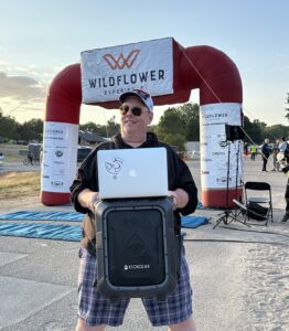 Pepper Daniels of 98.1 KJUG Radio and long time announcer at the Wildflower Experience holding a large portable speaker and laptop so he can announce and entertain ANYWHERE.