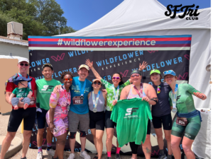 Photo of a group of SF Tri Club finishers with medals posing in front of a “#wildflowerexperience” backdrop. 