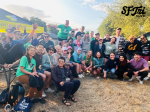 Photo of a group of SF Tri Club members gathered outdoors under a club tent, smiling and posing together. 